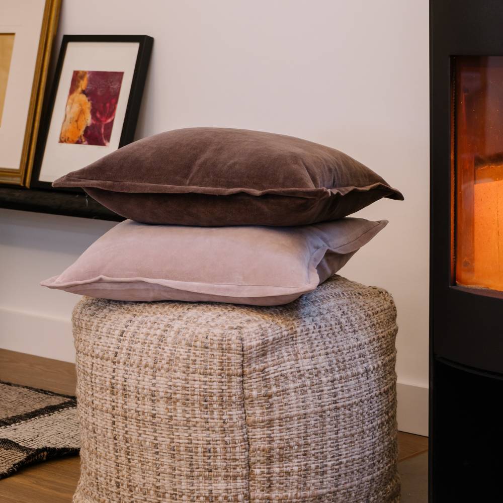 Two pillows stacked on a textured ottoman with framed artwork in the background.