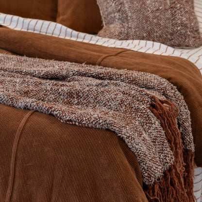 Brown textured blanket draped over a bed with pillows in a warm-toned room.
