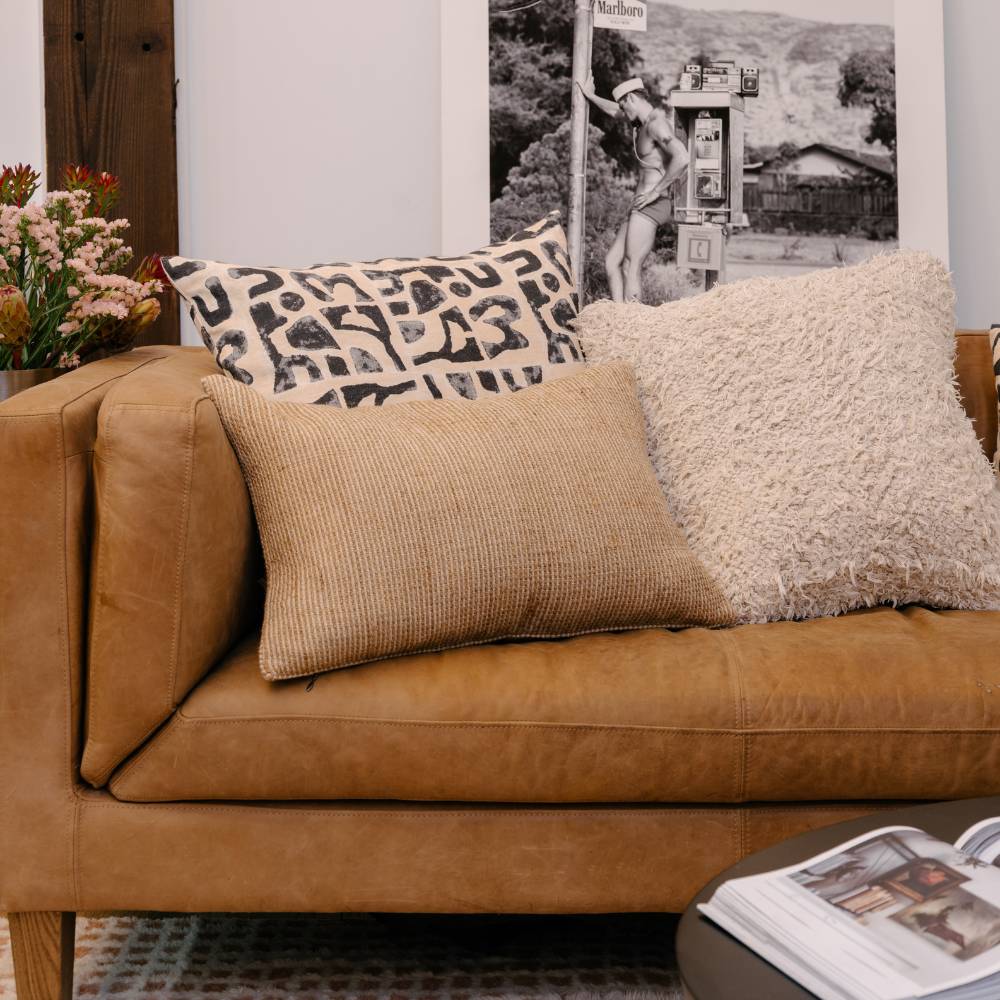 Brown leather sofa with patterned and textured cushions, floral arrangement, and framed picture in the background.