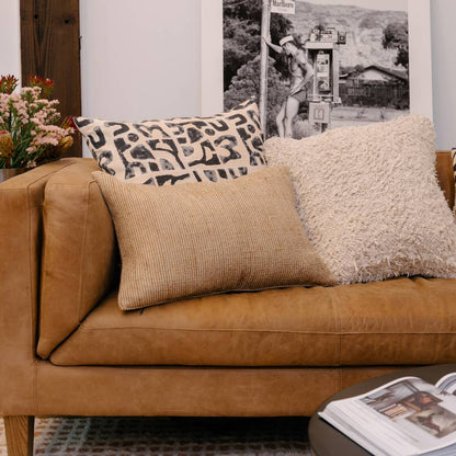 Brown leather sofa with patterned and textured cushions, floral arrangement, and framed picture in the background.