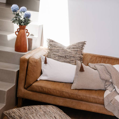 Brown leather sofa with decorative pillows and a vase of flowers on a staircase.