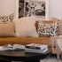 Brown sofa with patterned and fluffy pillows, books on a coffee table, and a framed picture in the background.