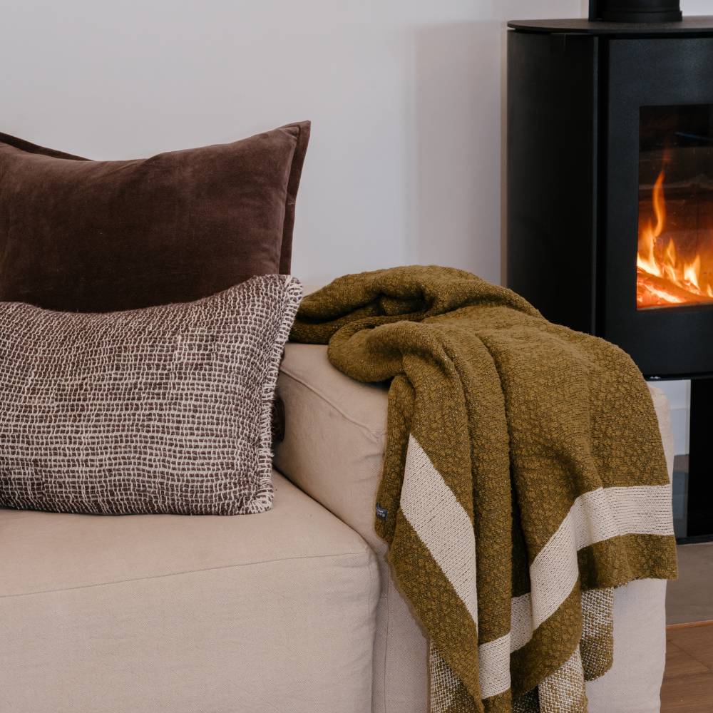 Cozy living room with a beige sofa, brown pillows, and a green blanket in front of a fireplace.