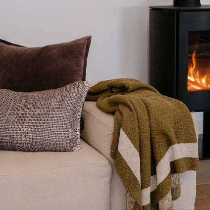 Cozy living room with a beige sofa, brown pillows, and a green blanket in front of a fireplace.