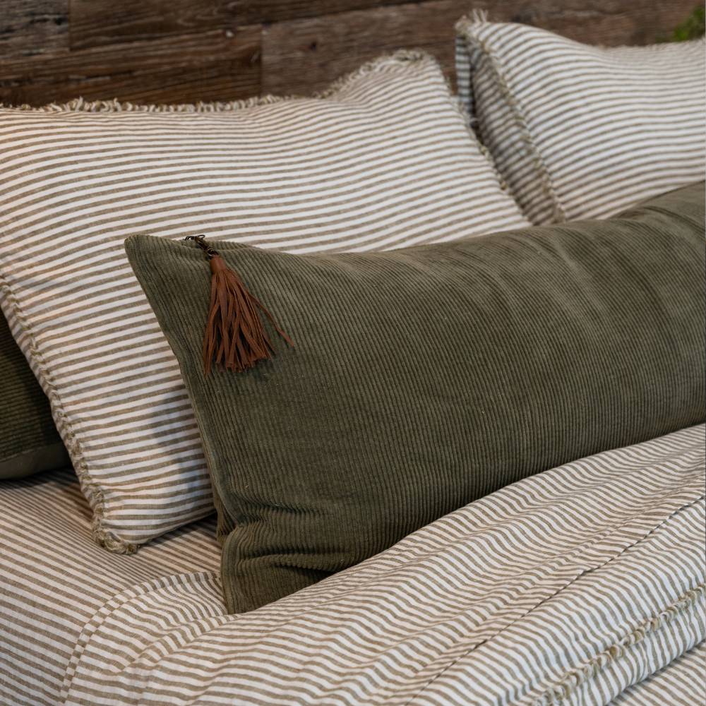 Green pillow with a tassel on a bed with striped bedding.
