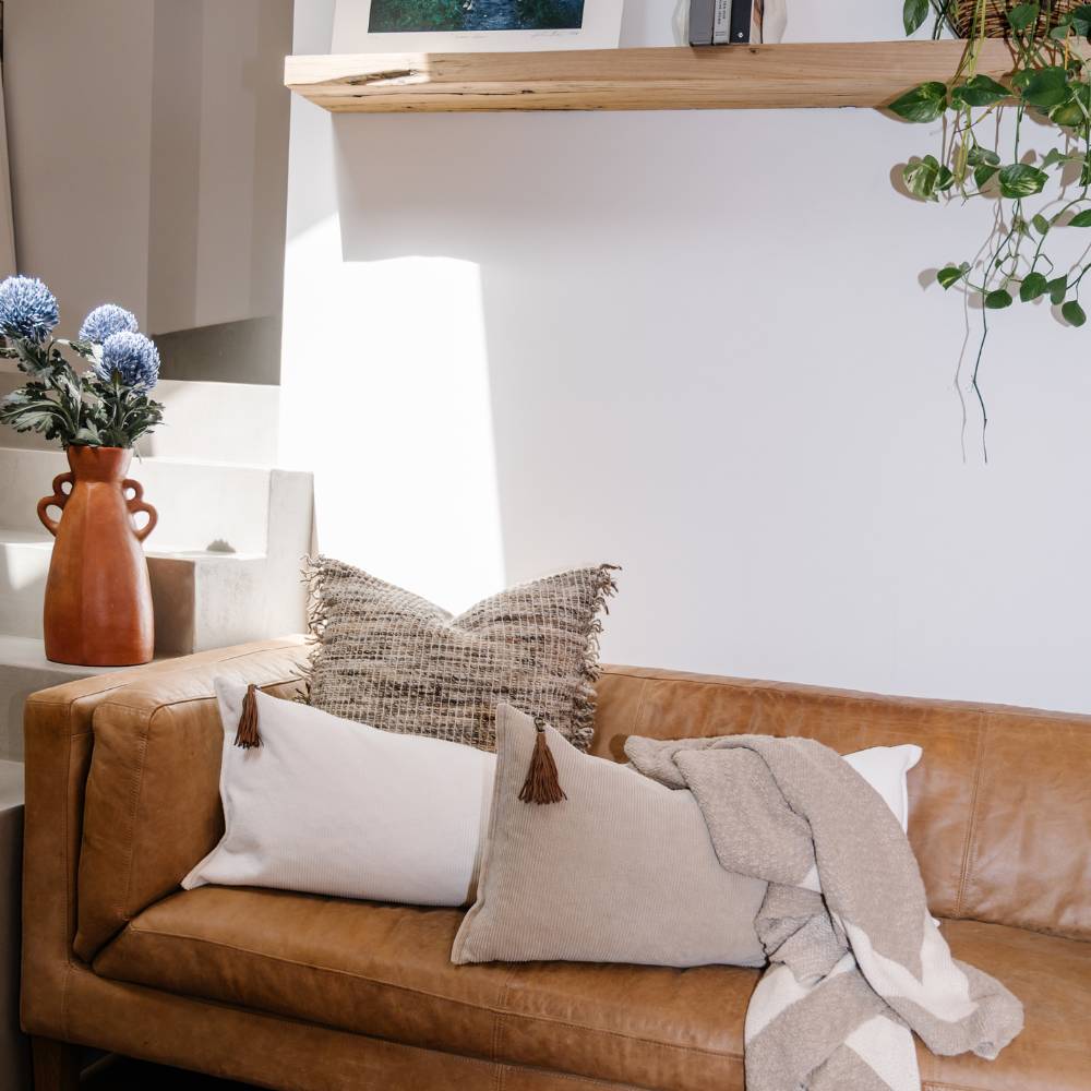 Brown leather sofa with decorative pillows and a blanket in a living room setting.