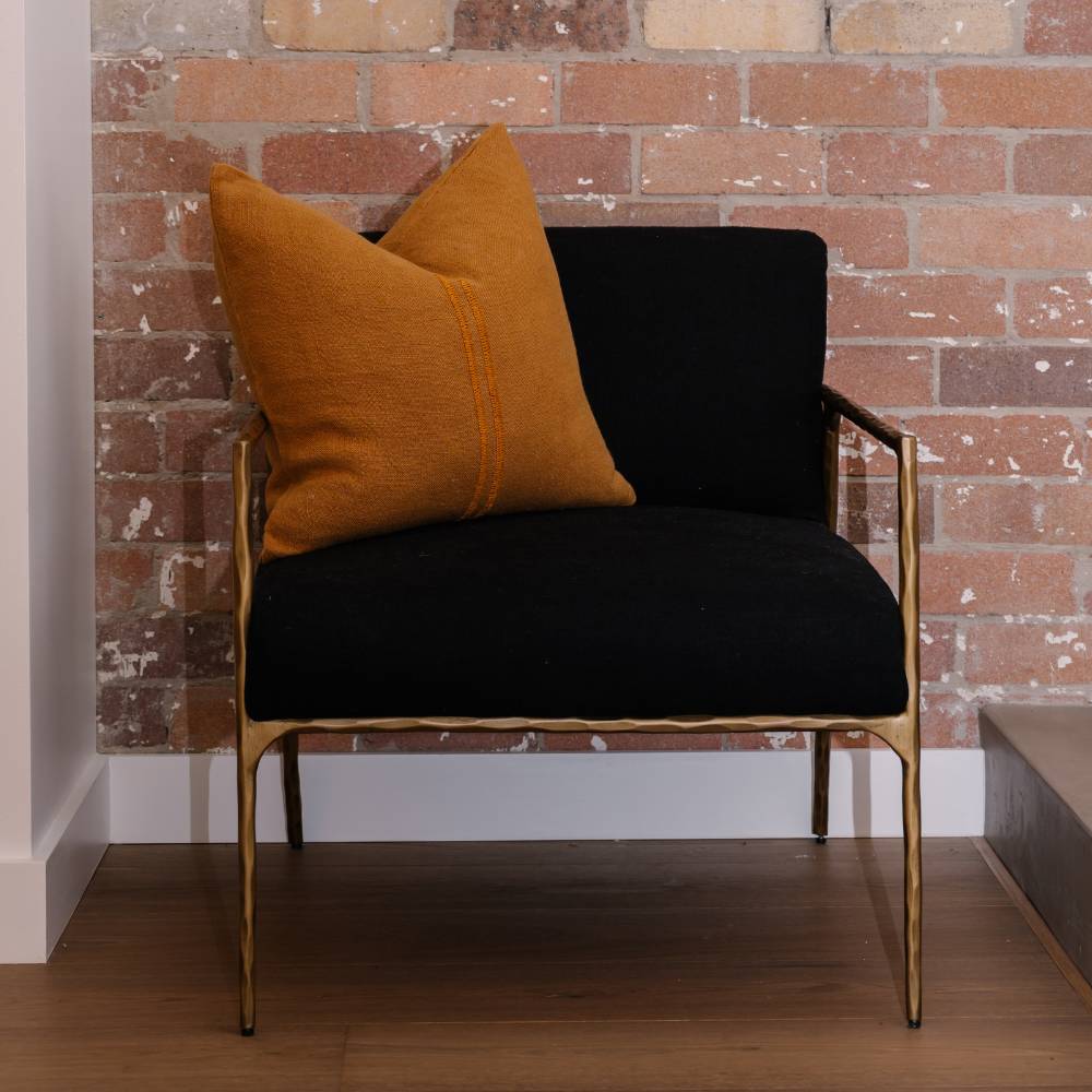 Black armchair with orange cushions against a brick wall.
