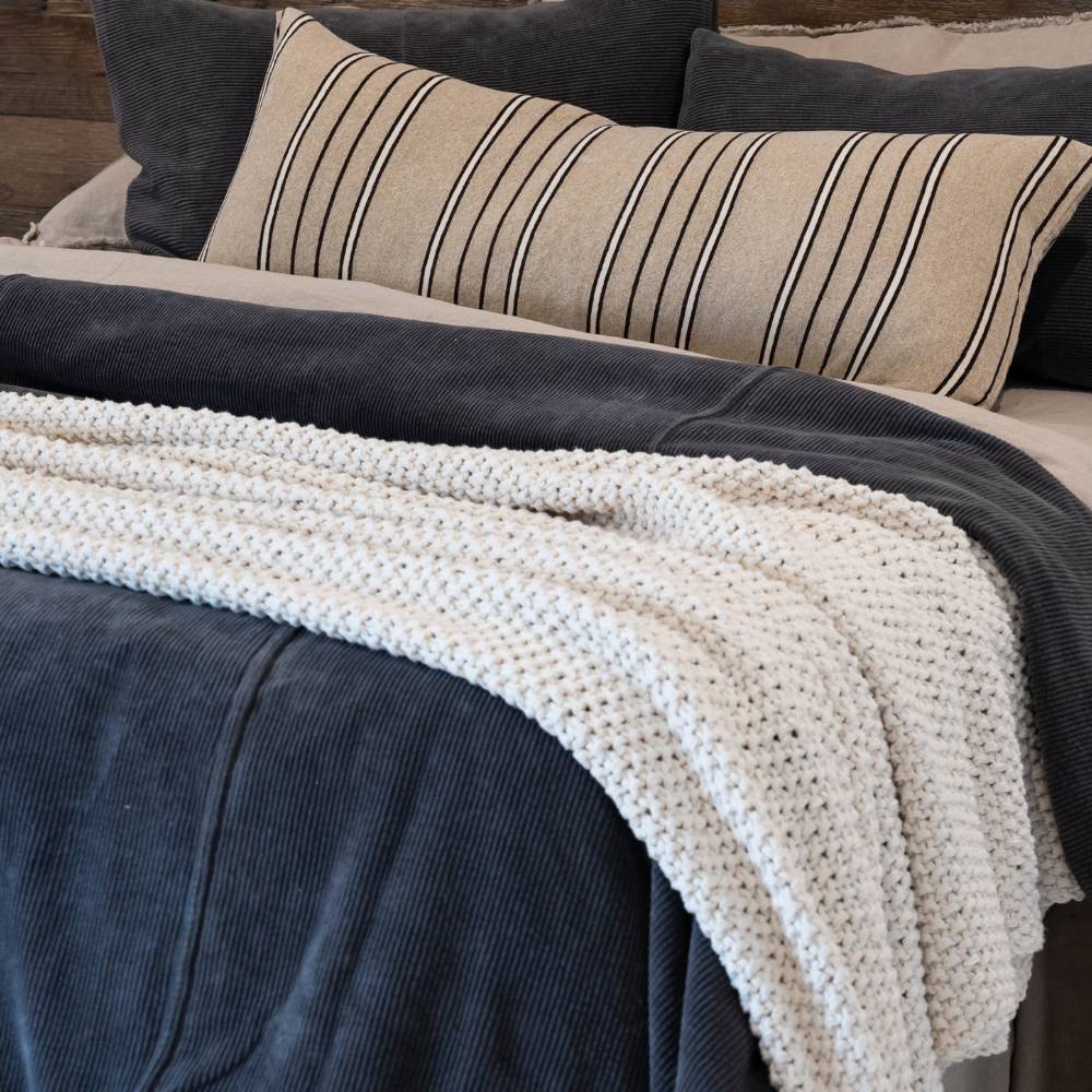 Cozy bed with striped pillow, dark blue blanket, and white knit throw.