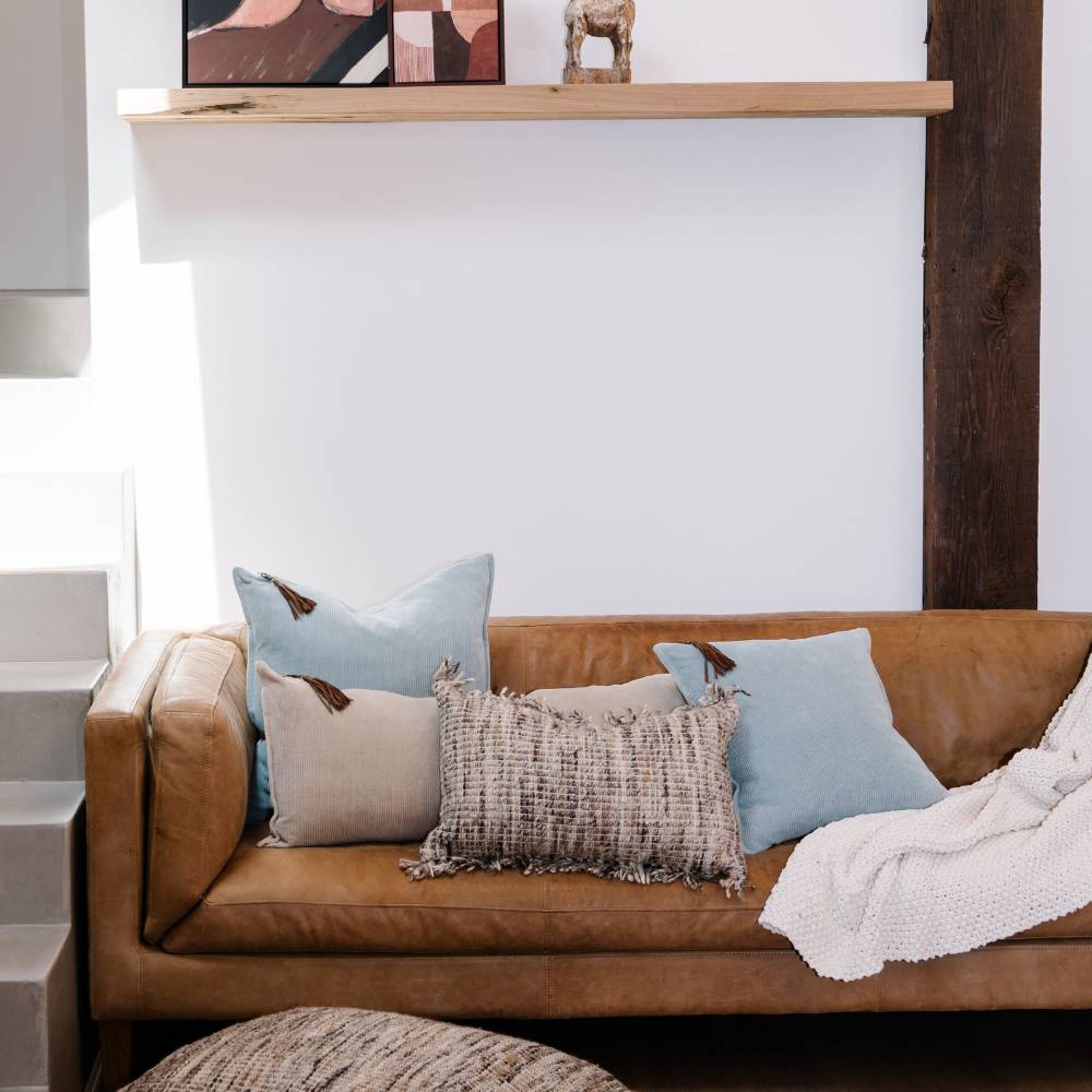 Brown leather sofa with decorative pillows and a blanket in a living room setting.