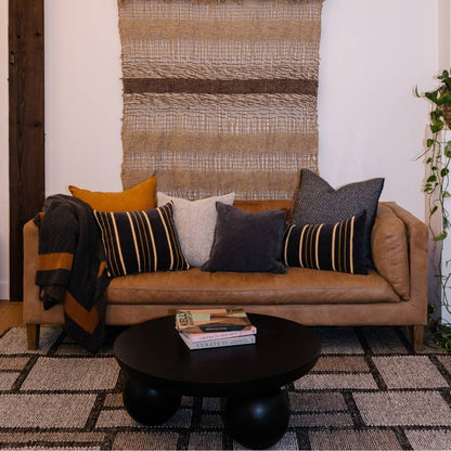 Brown leather sofa with decorative pillows and a black coffee table in a living room setting.