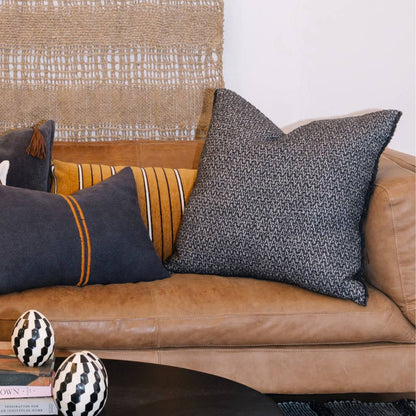 Decorative pillows on a brown leather sofa with a textured wall in the background