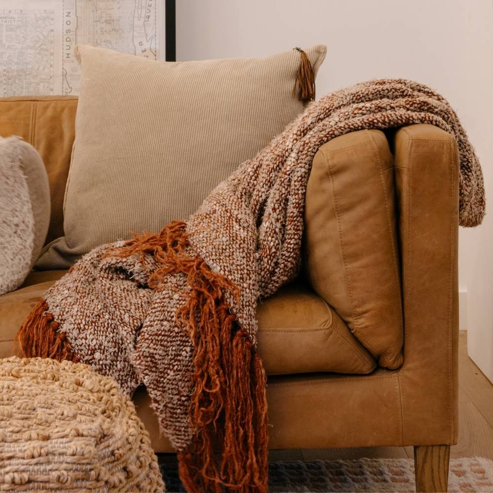 Brown leather sofa with textured blanket and pillows in a cozy living room setting.