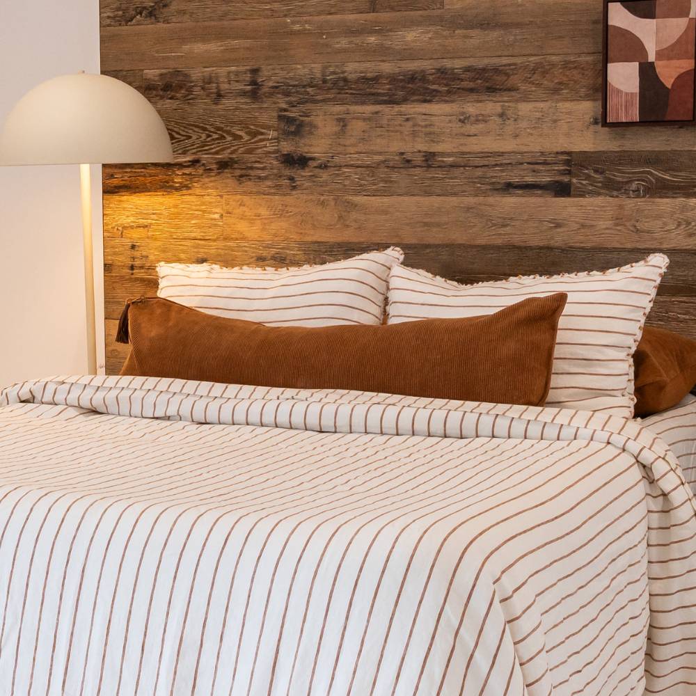 Bed with striped bedding and pillows against a wooden wall.