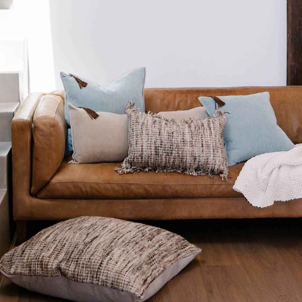 Brown leather sofa with decorative pillows and a blanket in a living room setting.