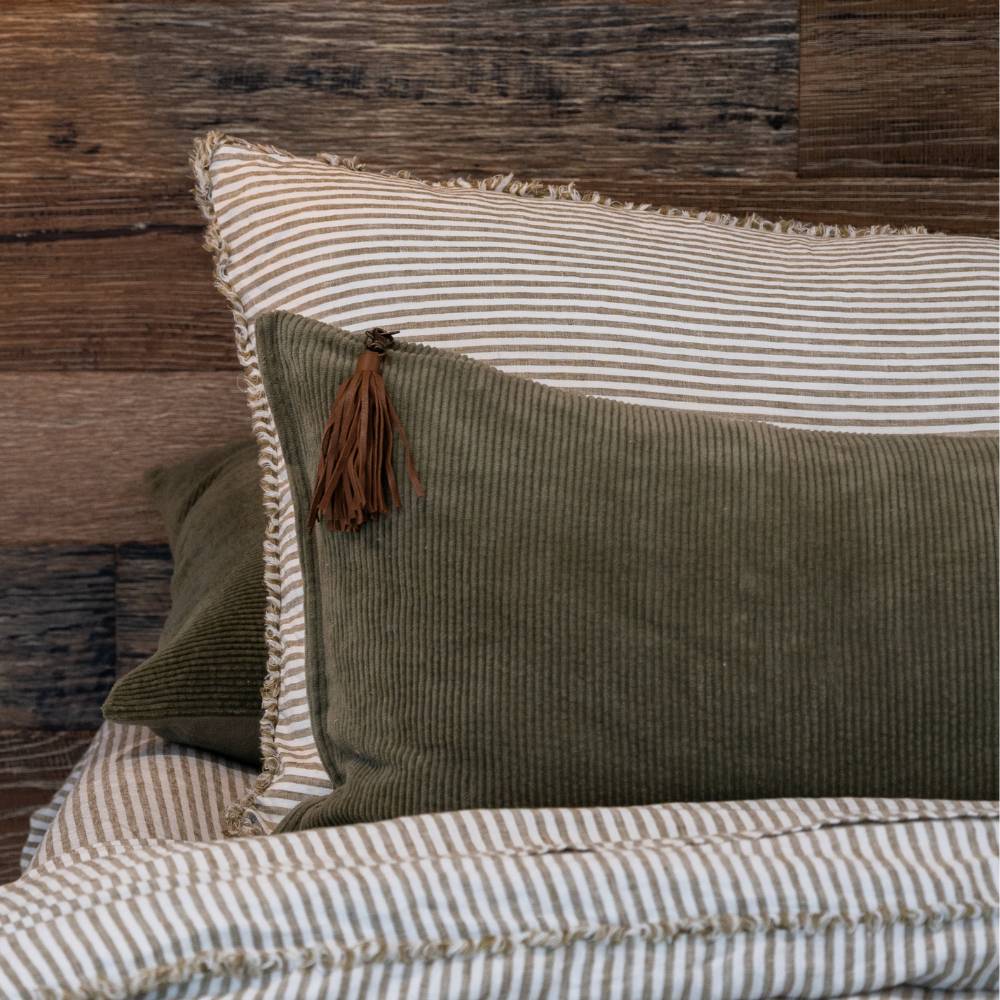 Two pillows, one green and one striped, on a bed with a wooden headboard.