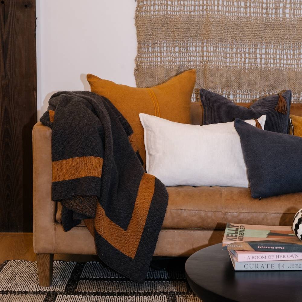 Brown sofa with colorful pillows and a blanket, accompanied by books on a small table.