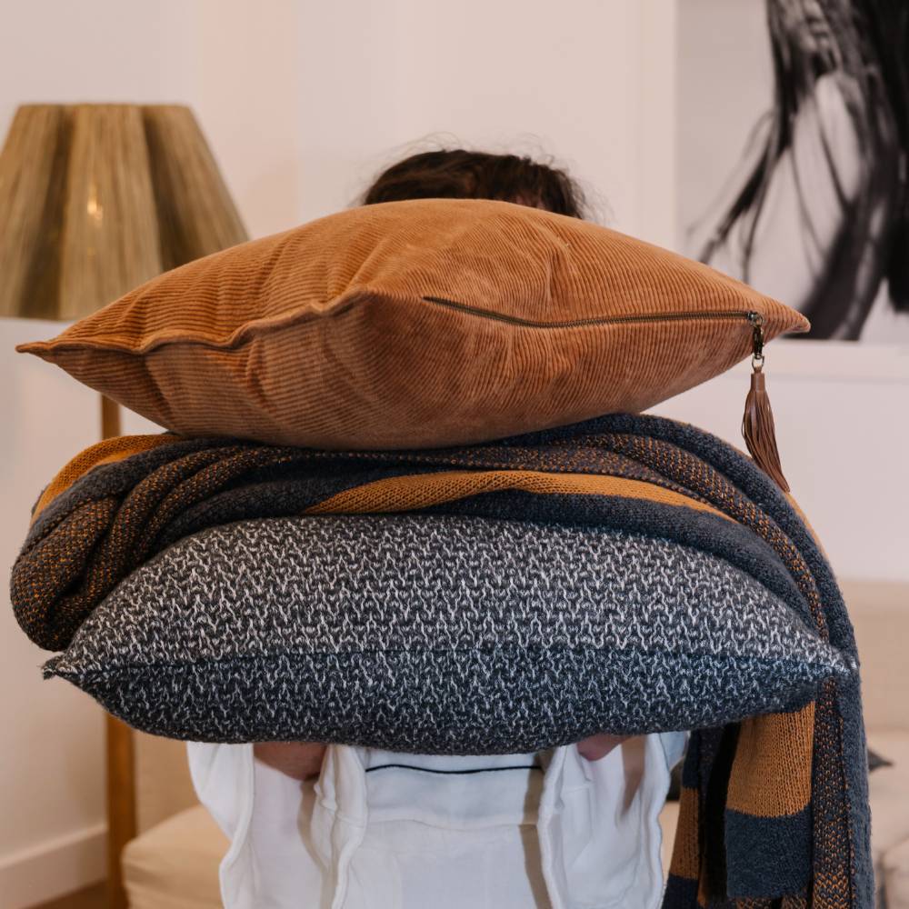 Person holding a stack of pillows and blankets with a blurred background