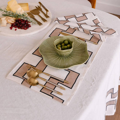 Table setting with green bowl, gold cutlery, and patterned placemats on a white tablecloth.