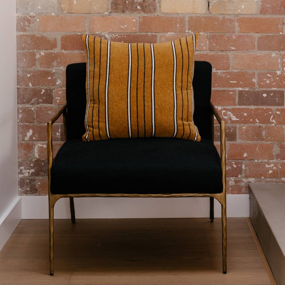 Brown striped pillow on a chair with black seat against a brick wall