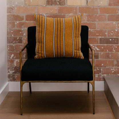 Brown striped pillow on a chair with black seat against a brick wall