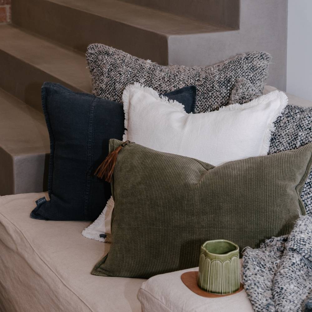 Assorted pillows on a sofa with a decorative plant on a small table.