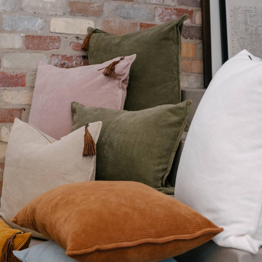 Assorted colorful pillows on a sofa against a brick wall.