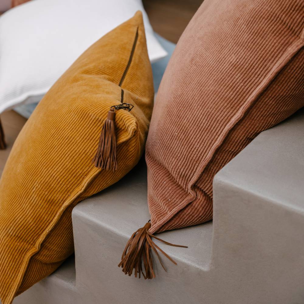 Two corduroy pillows with tassels on a concrete surface