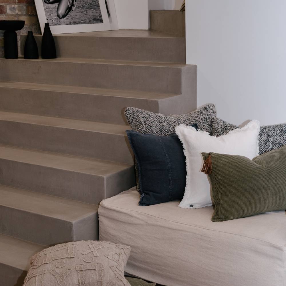 Gray sofa with patterned cushions against a staircase in a home setting
