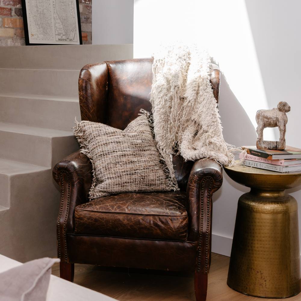 Brown leather armchair with a pillow and blanket in a room with a staircase.