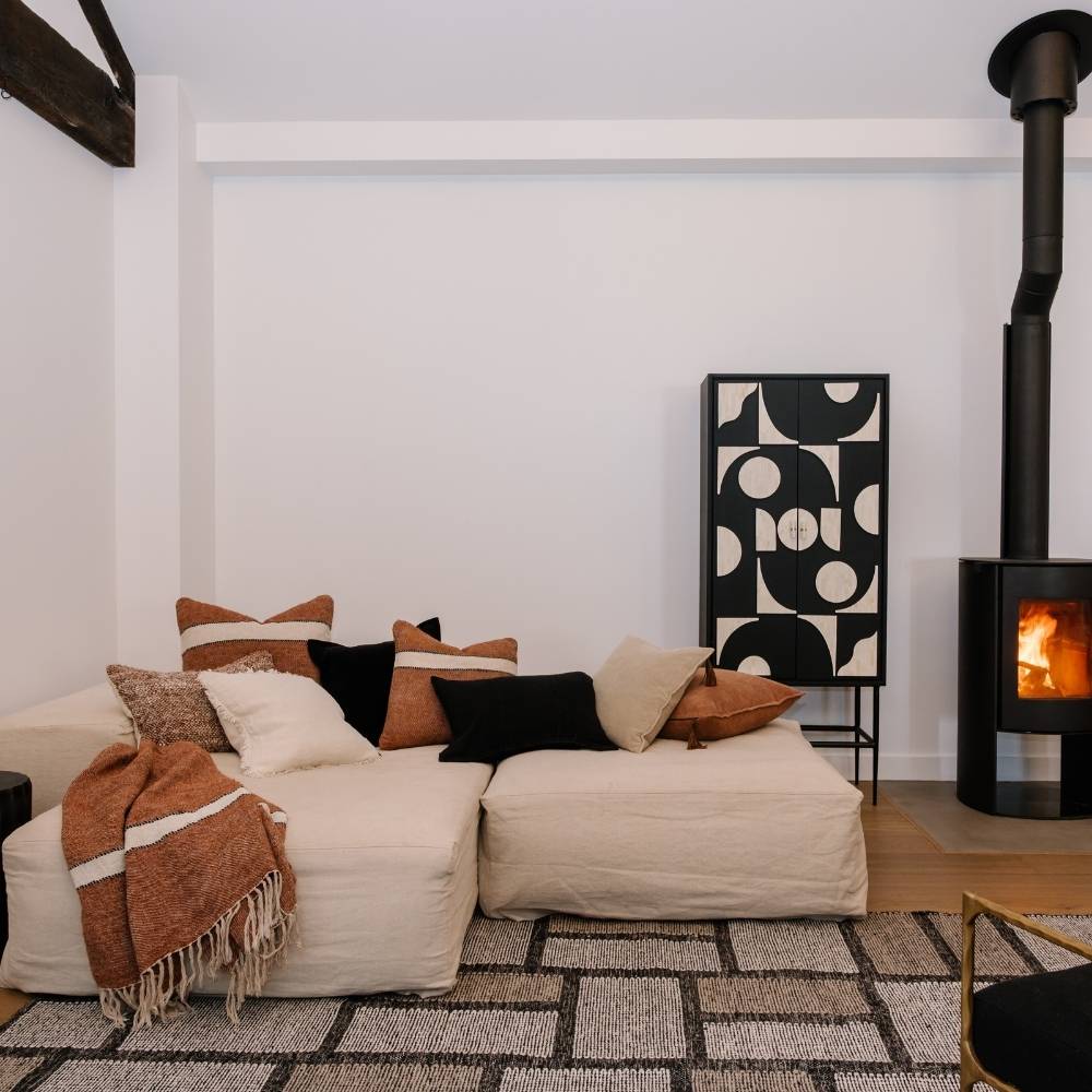 Cozy living room with a white sofa, patterned rug, and wooden stove.