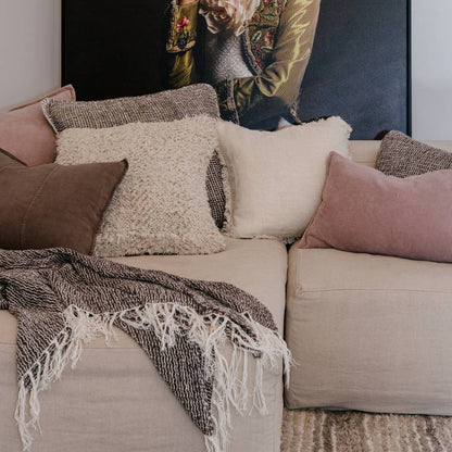 Beige sofa with decorative pillows and a throw, with a portrait of a person in the background.