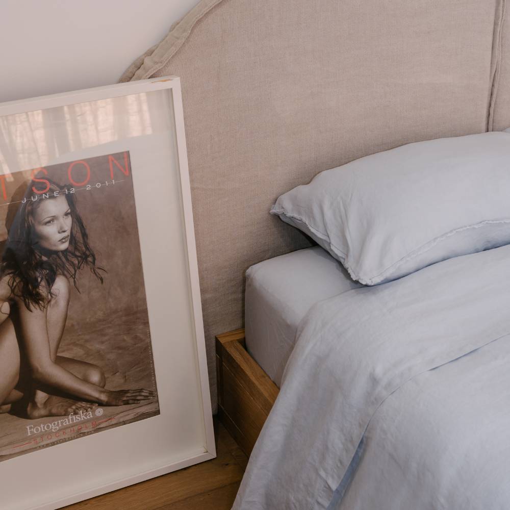 Framed magazine on a nightstand next to a bed with light blue bedding.