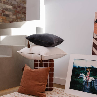 Three pillows stacked on a small table with a photograph of a person on a horse in the background.