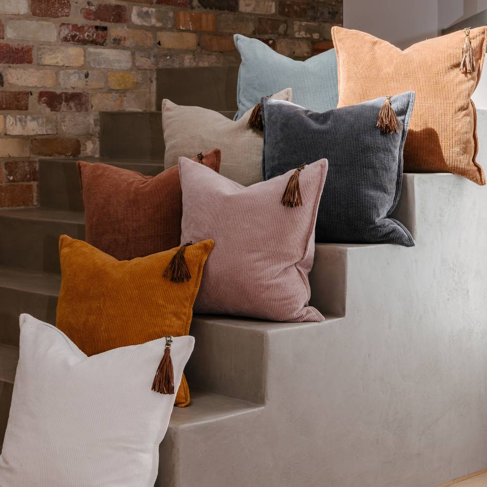 Colorful pillows with tassels arranged on a stone ledge against a brick wall.