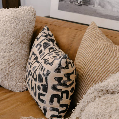 Patterned pillow on a brown leather sofa with other decorative pillows.