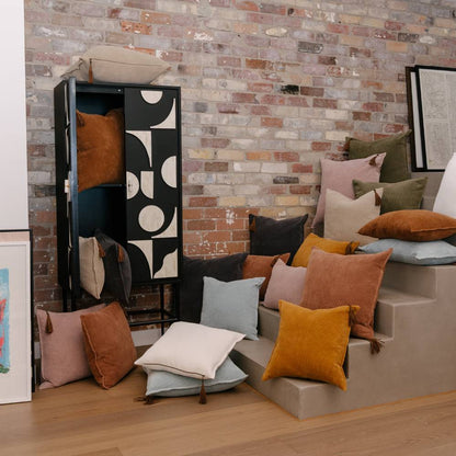 Colorful pillows on a stone ledge against a brick wall with a patterned cabinet.