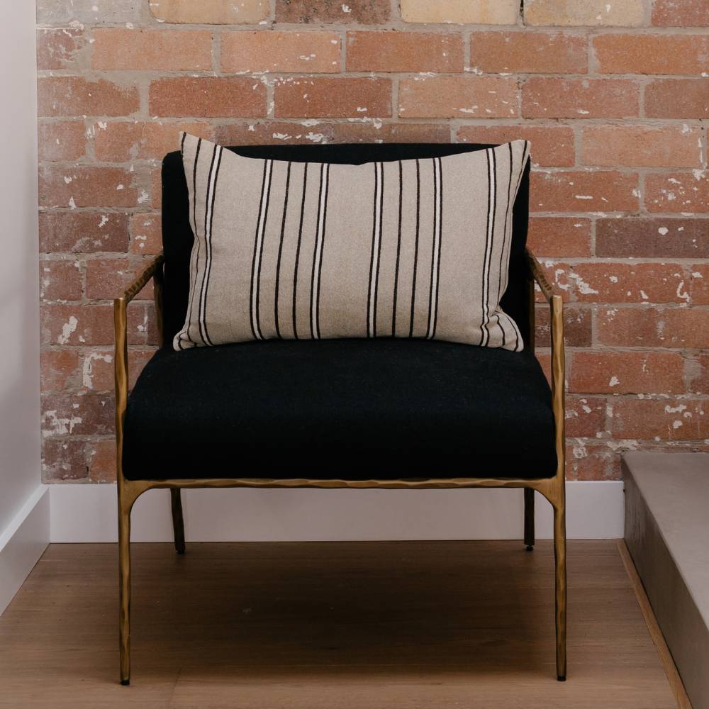 Chair with a beige striped pillow against a brick wall