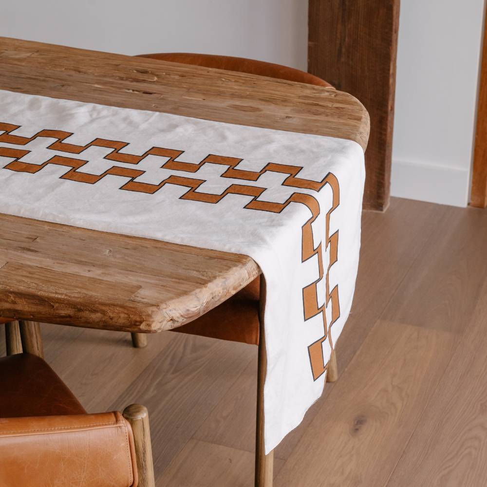 Wooden table with a white table runner featuring nutmeg geometric patterns