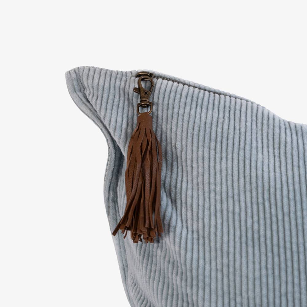 Light blue cushion with a brown leather tassel on a white background
