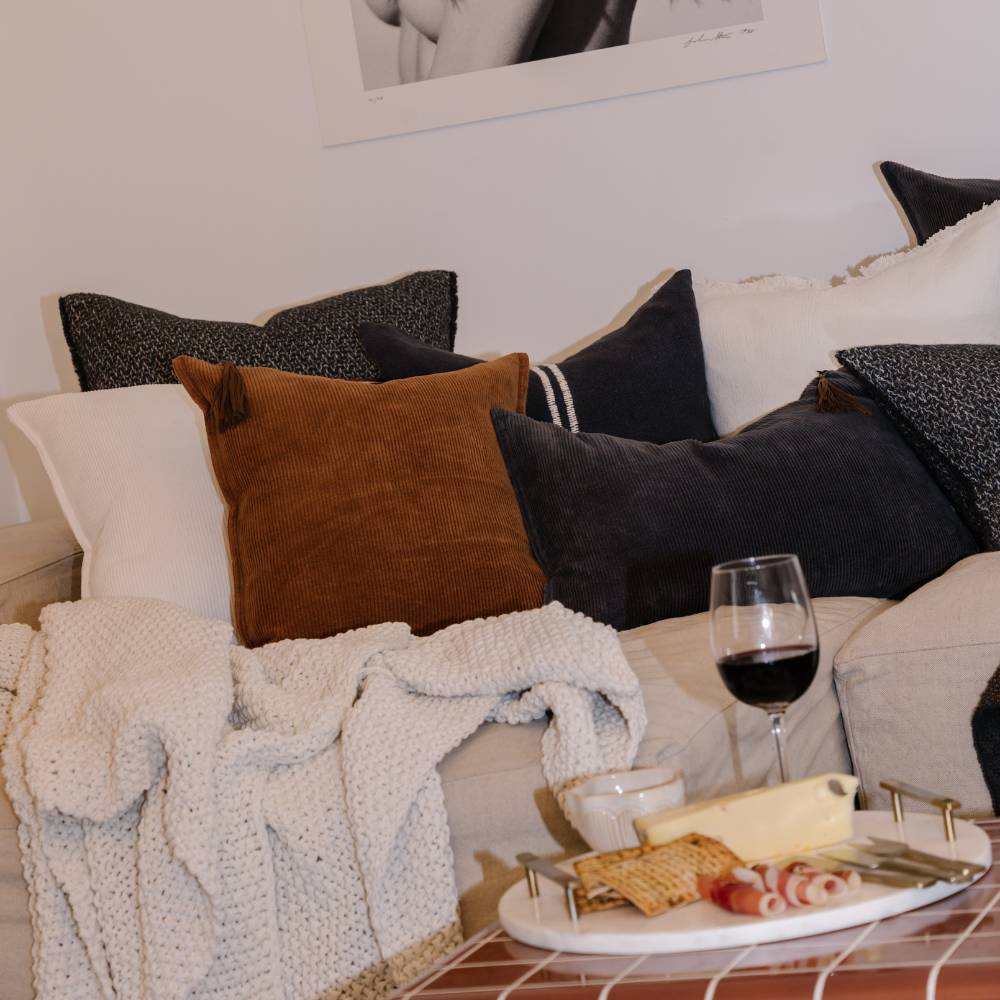 Cozy living room with pillows, a blanket, and a glass of red wine on a coffee table.