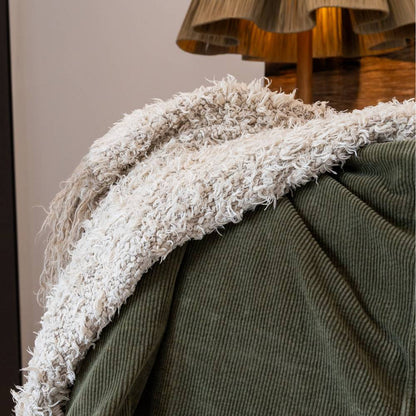 Close-up of a green textured blanket with white fringes draped over a surface.