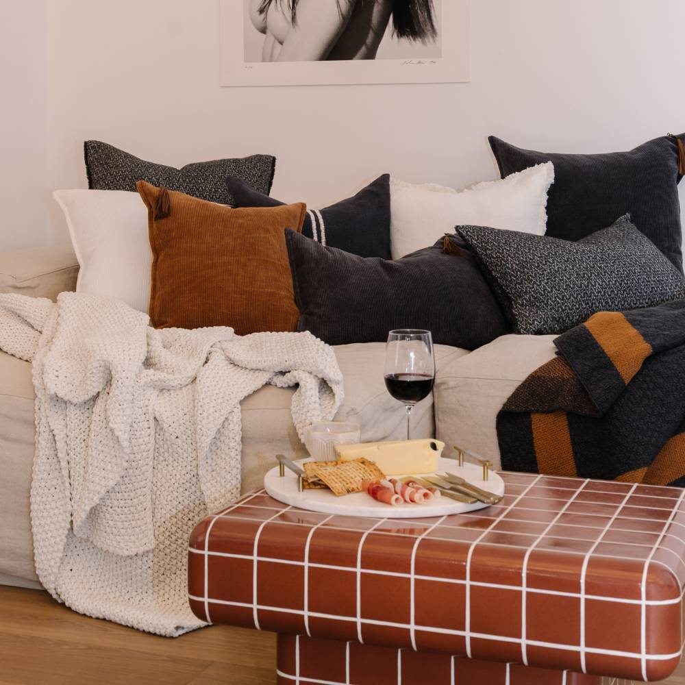 Cozy living room with a couch, pillows, blanket, and a small table with snacks and wine.
