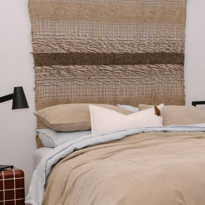 Bed with beige bedding and pillows against a textured woven headboard.