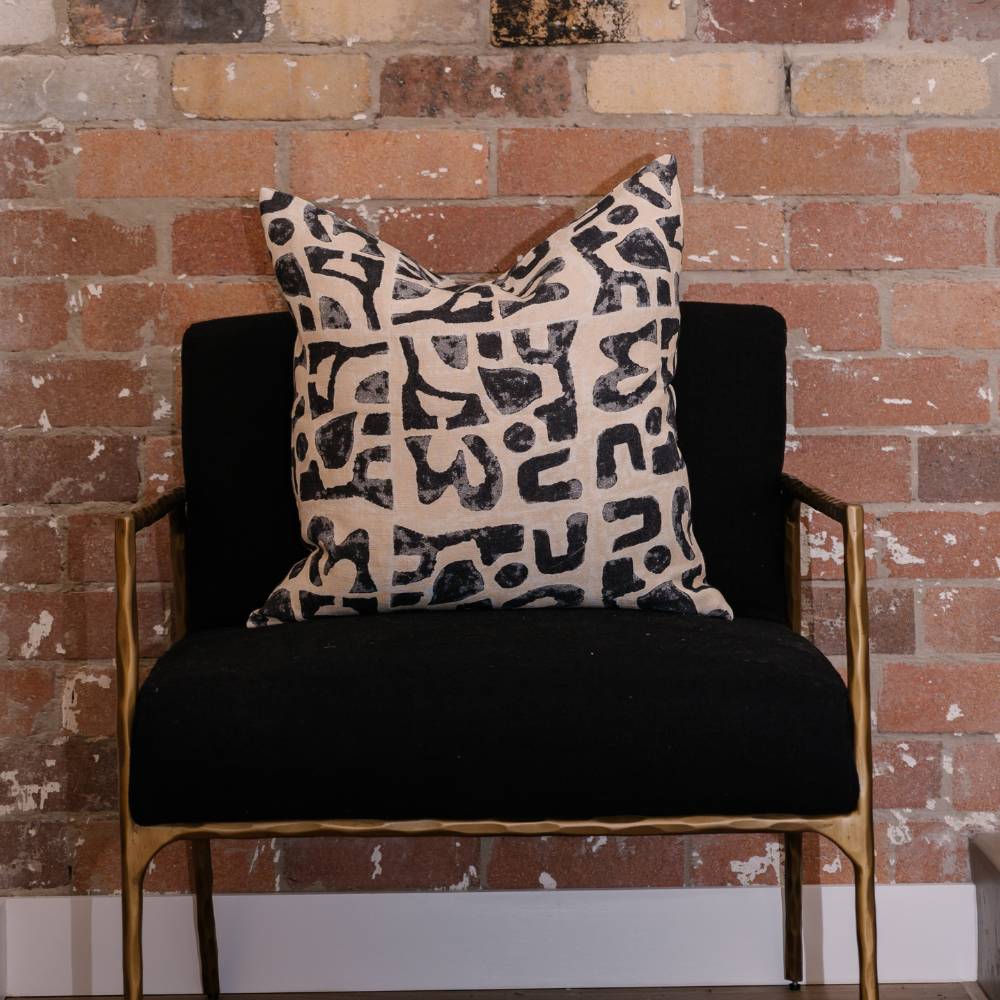 Black armchair with a patterned pillow against a brick wall