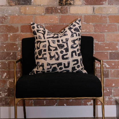Black armchair with a patterned pillow against a brick wall