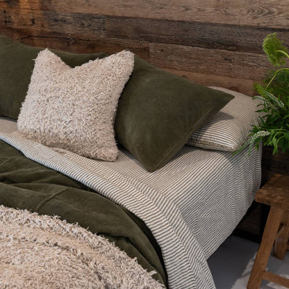 Bed with green and beige pillows and a blanket against a wooden wall.