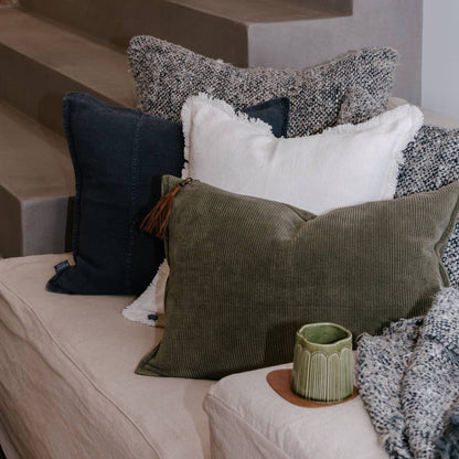 Decorative pillows on a sofa with a small green pot on a table.