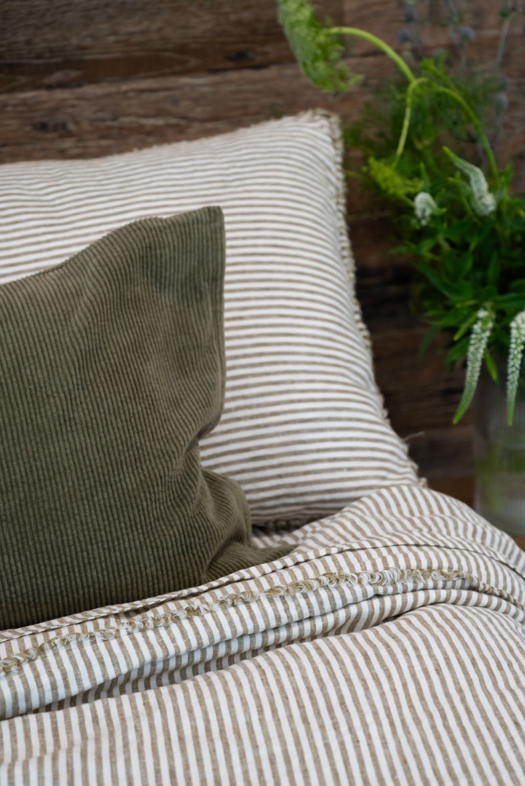 Striped linen bedding with a moss green pillow on a wooden surface