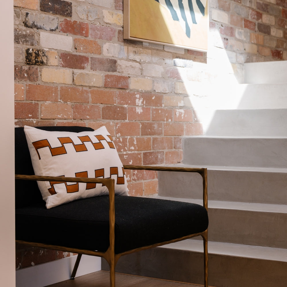 Pillow with a geometric interlocking pattern on a black chair against a brick wall