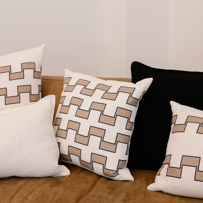 Decorative pillows on a brown leather couch: three with interlocking beige/white geometric patterns, one solid white, one black.